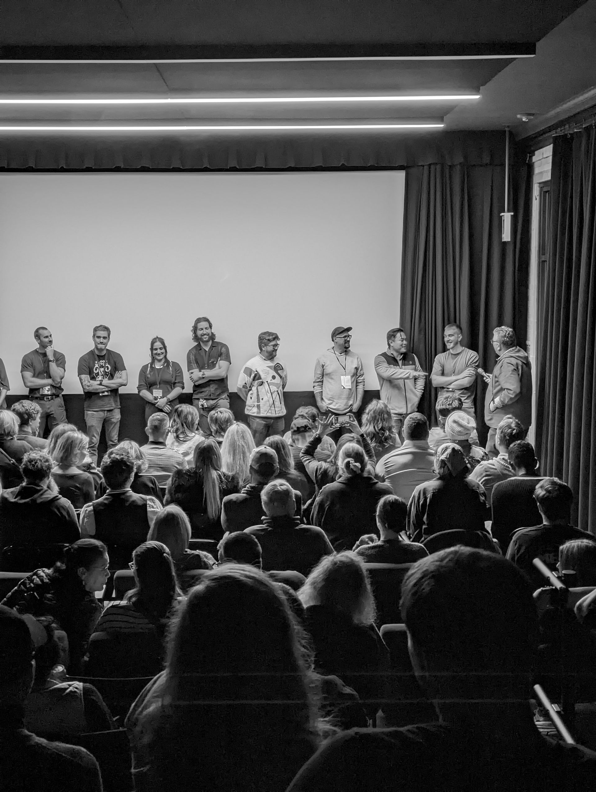 Panel of people on stage in front of a seated audience at an event. Black and white.