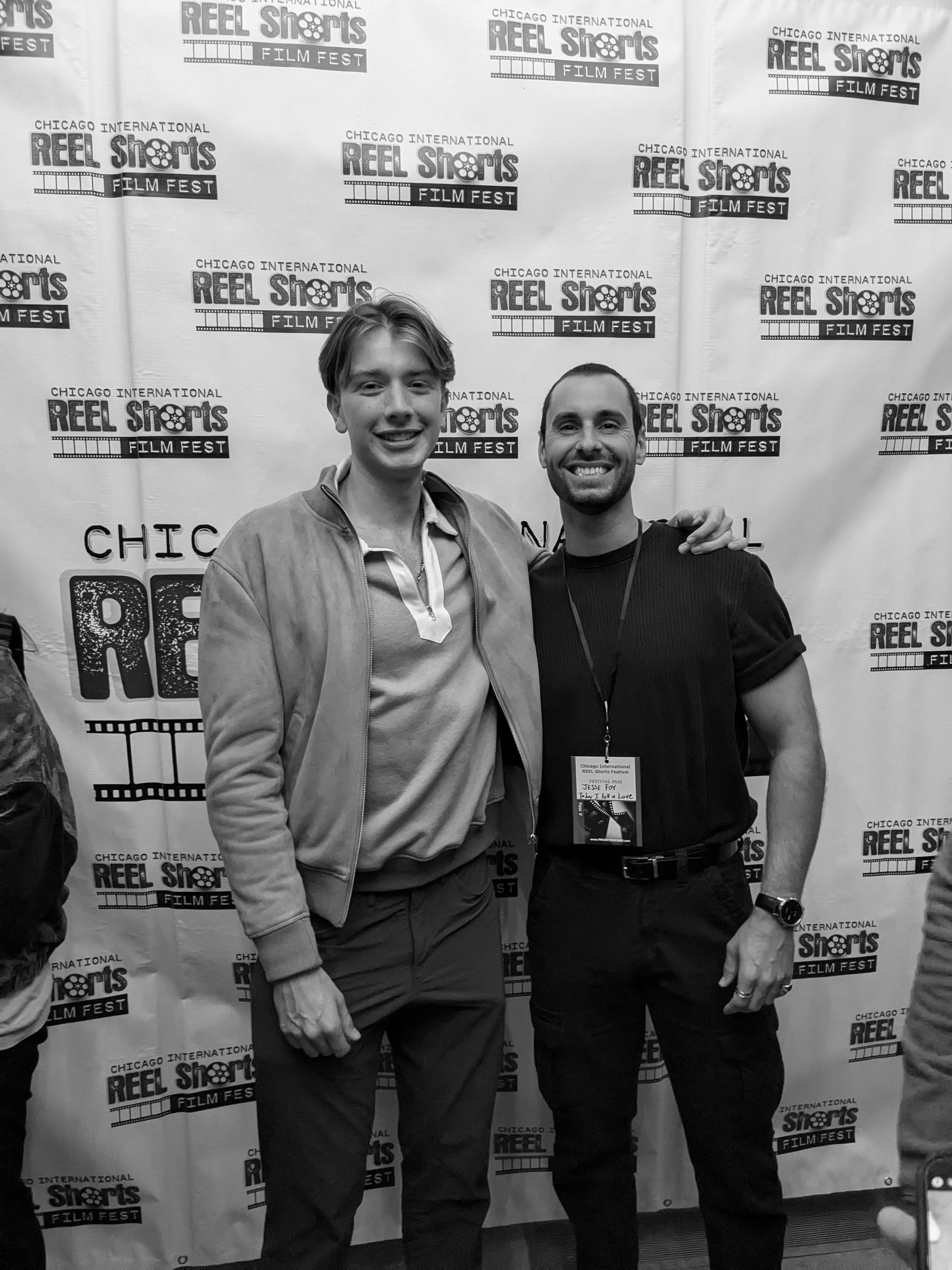 Two men pose for photo at Reel Shorts Film Fest; one in jacket, the other in black shirt has arm around the first.
