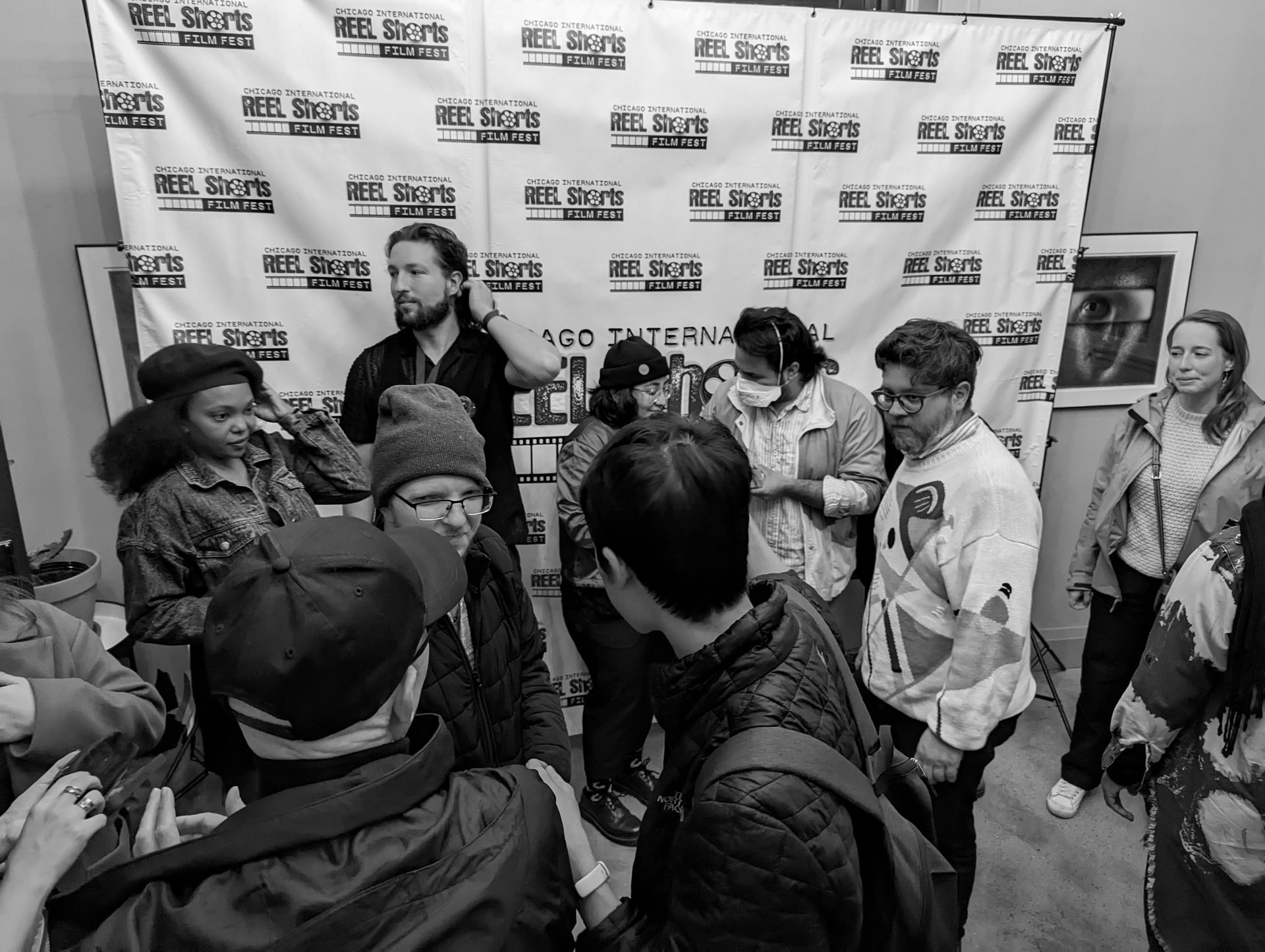 Group of people gathered, likely at an event. Individuals are interacting near a banner. Black and white photo.