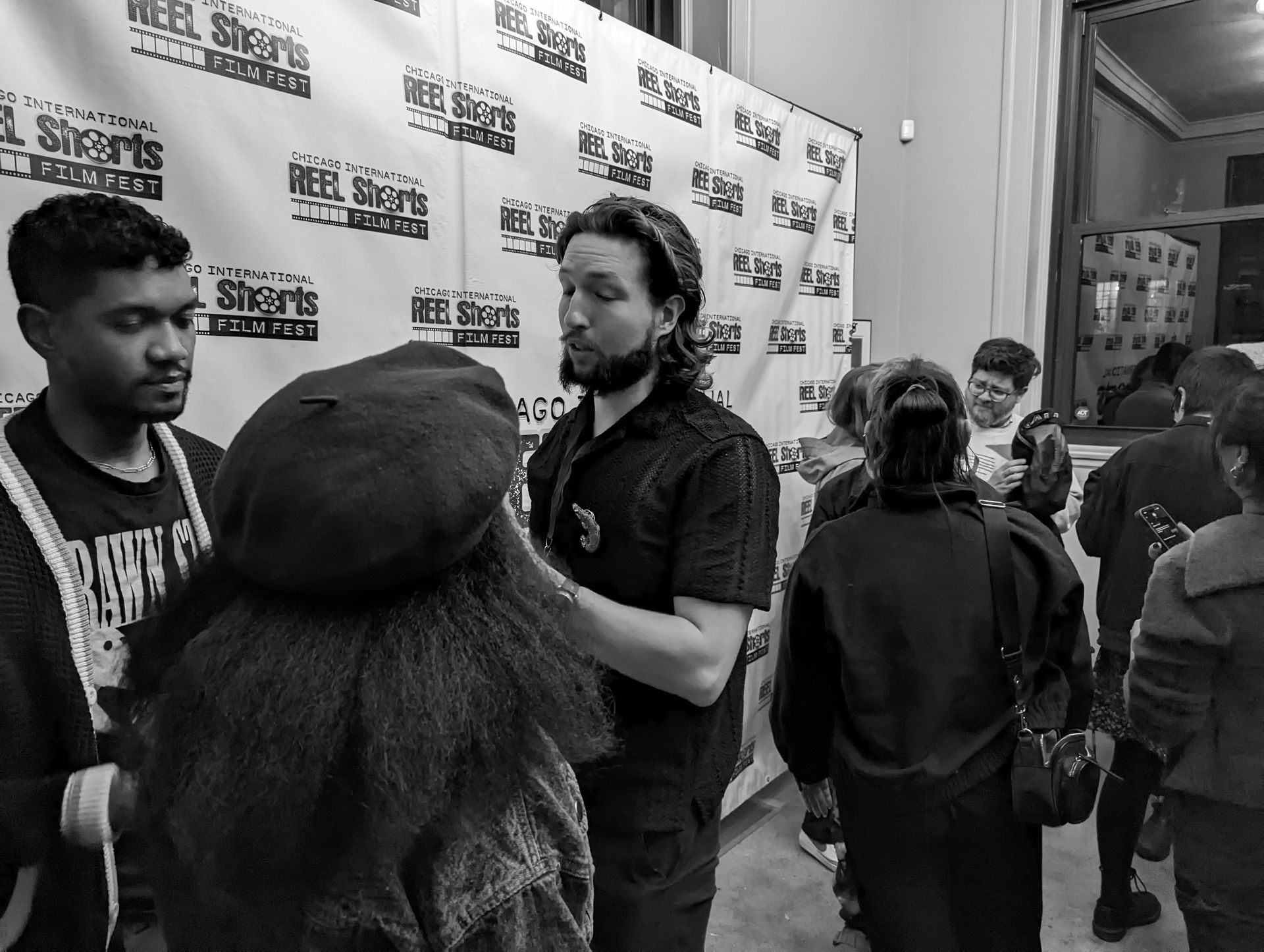 People at an event, conversing in front of a branded backdrop. Black and white photo.