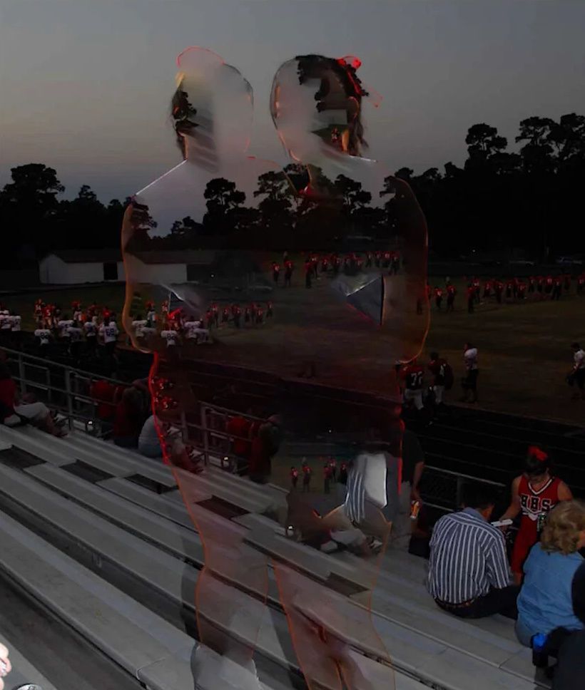 People in bleachers watching a football game at dusk.