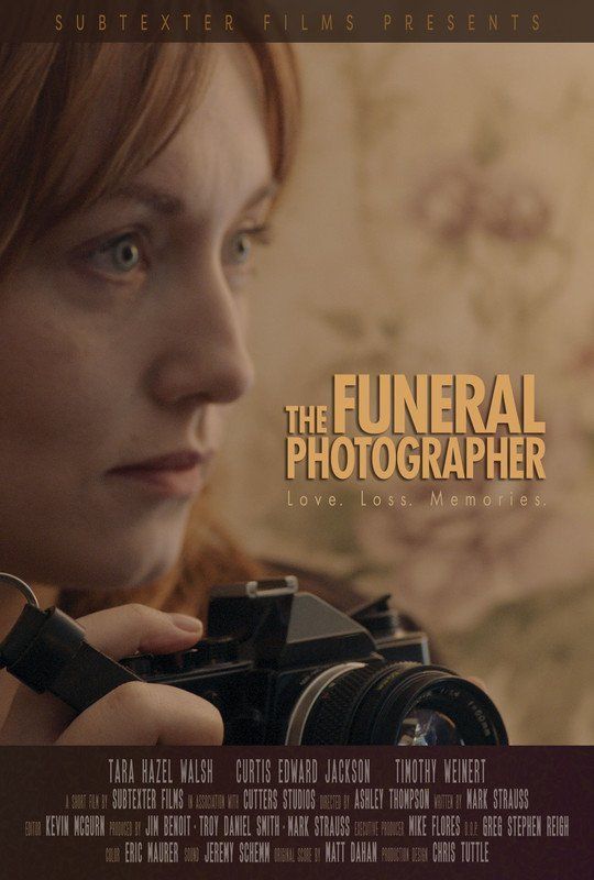Woman with red hair, holding camera, looks somber; text