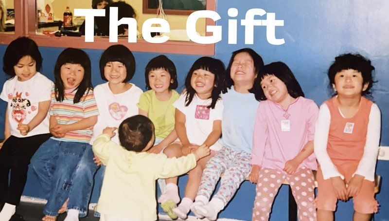 Group of children, seated and smiling, with a toddler reaching towards them; blue background.