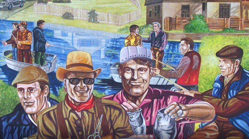 Men fishing from boats and the shore, smiling. Waterfront scene, some in brown clothing.