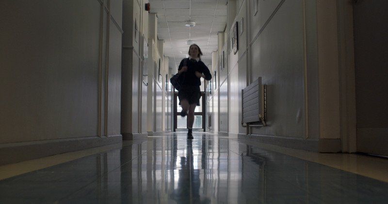 Girl running down a school hallway. Dark silhouette against bright end of the hall.