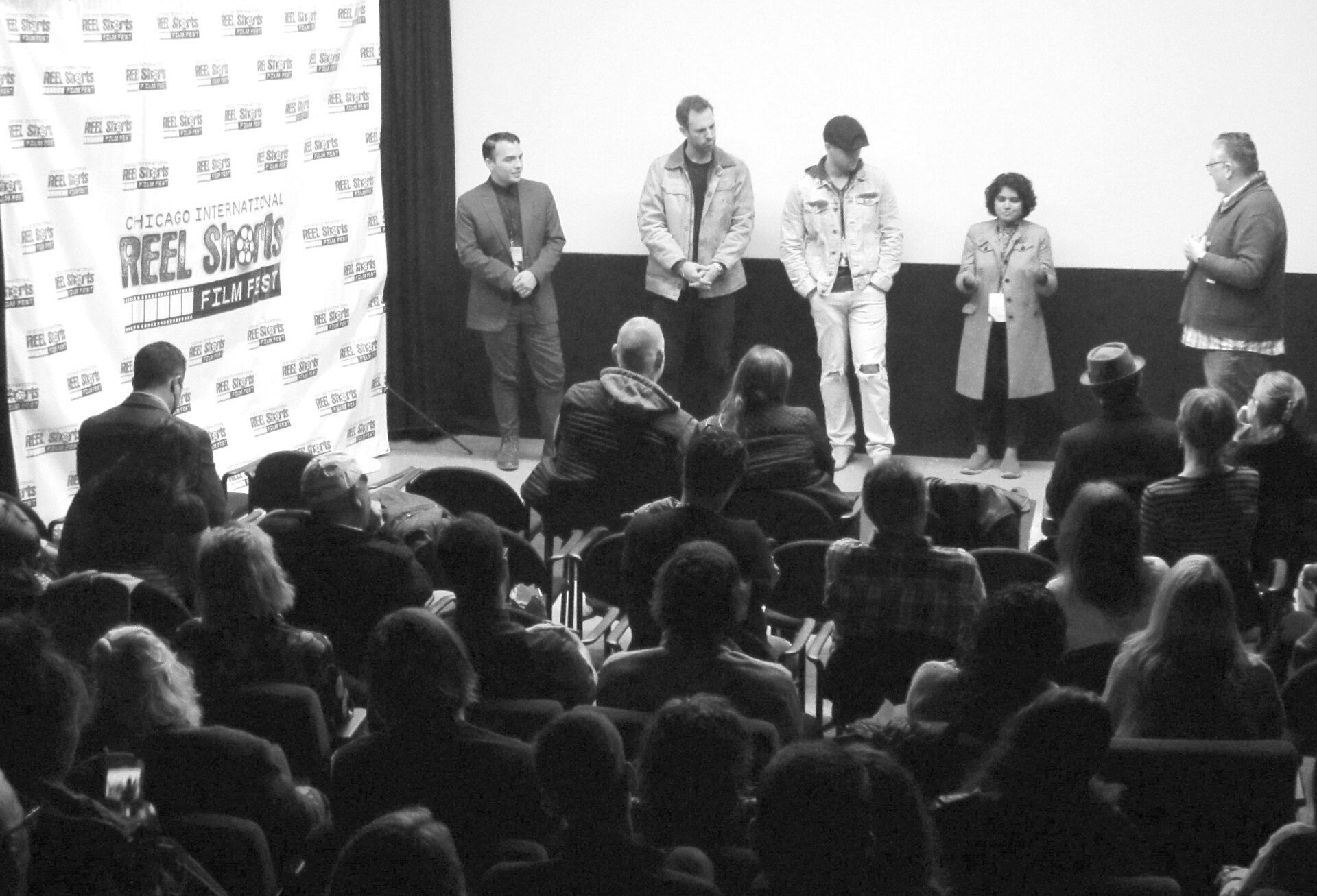 Audience watches people on stage at a film festival. Black and white.