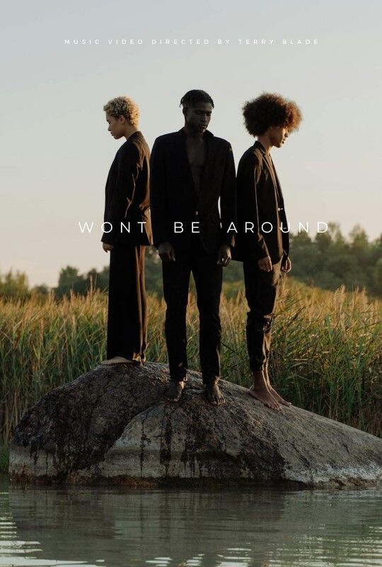 Three people in black suits standing on a rock in water; text