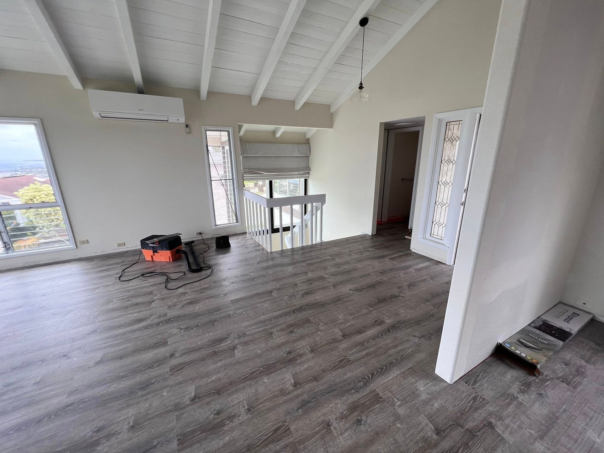Spacious room with gray wood floors, white walls, and a staircase. A/C unit and doorway visible.