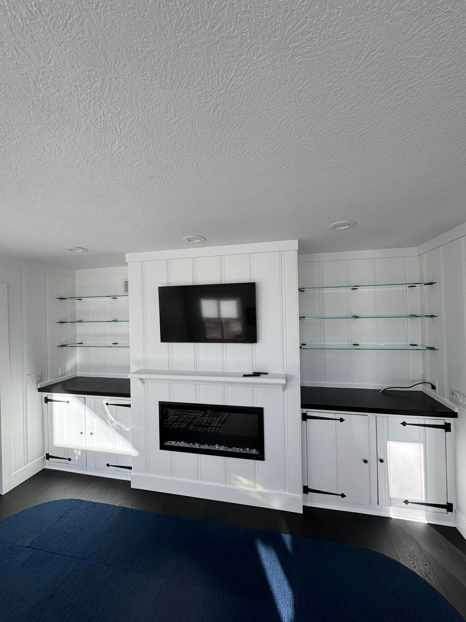 White built-in entertainment center with fireplace, TV, black countertops, and floating shelves.