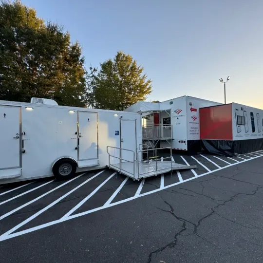 White utility trailers and a red trailer parked in a striped lot at dusk, with trees in the background