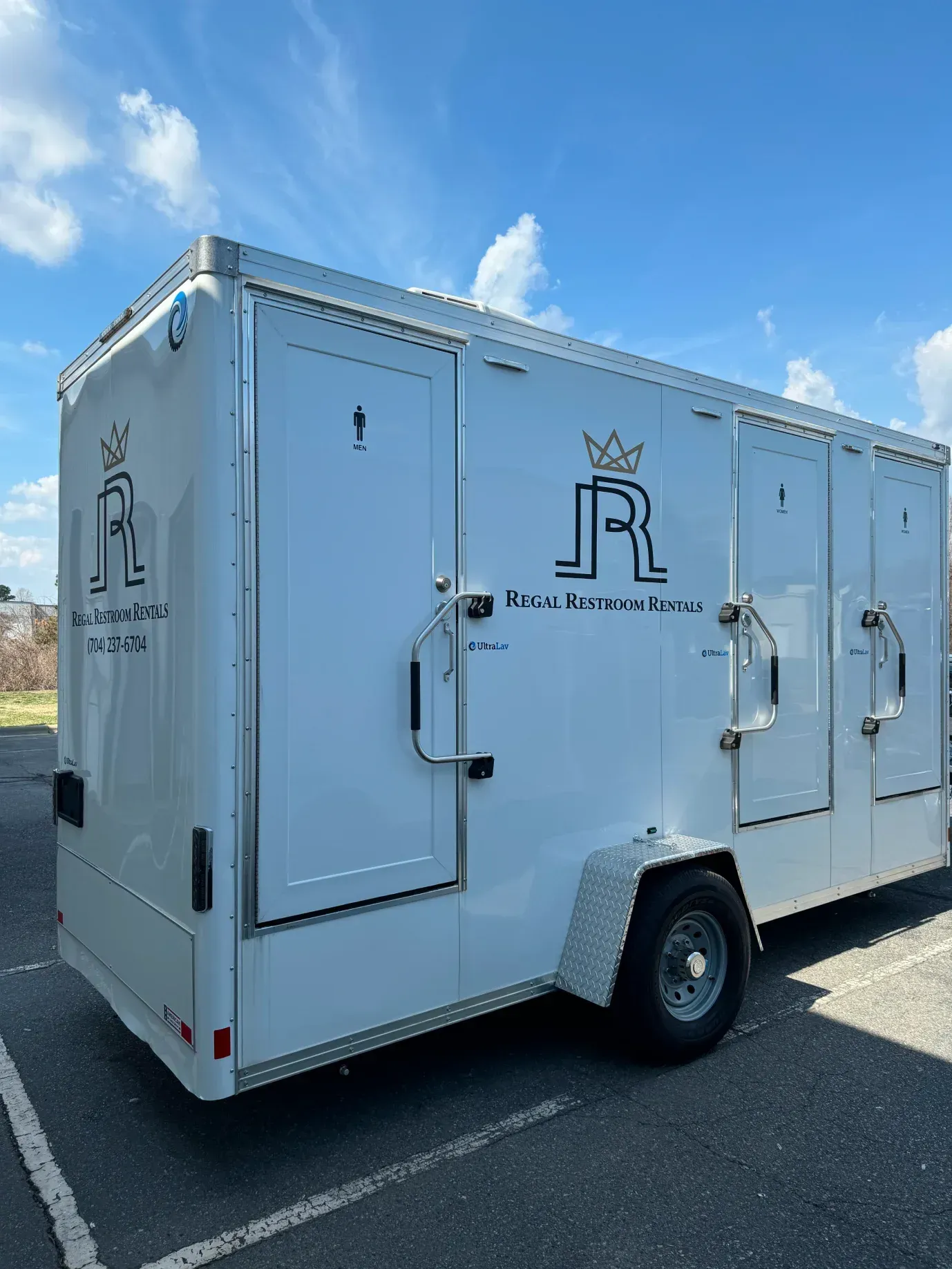 White enclosed cargo trailer with logo, parked in a lot under a blue sky.