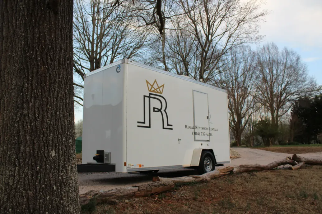 White logo-covered trailer parked by trees on a roadside in a park-like setting