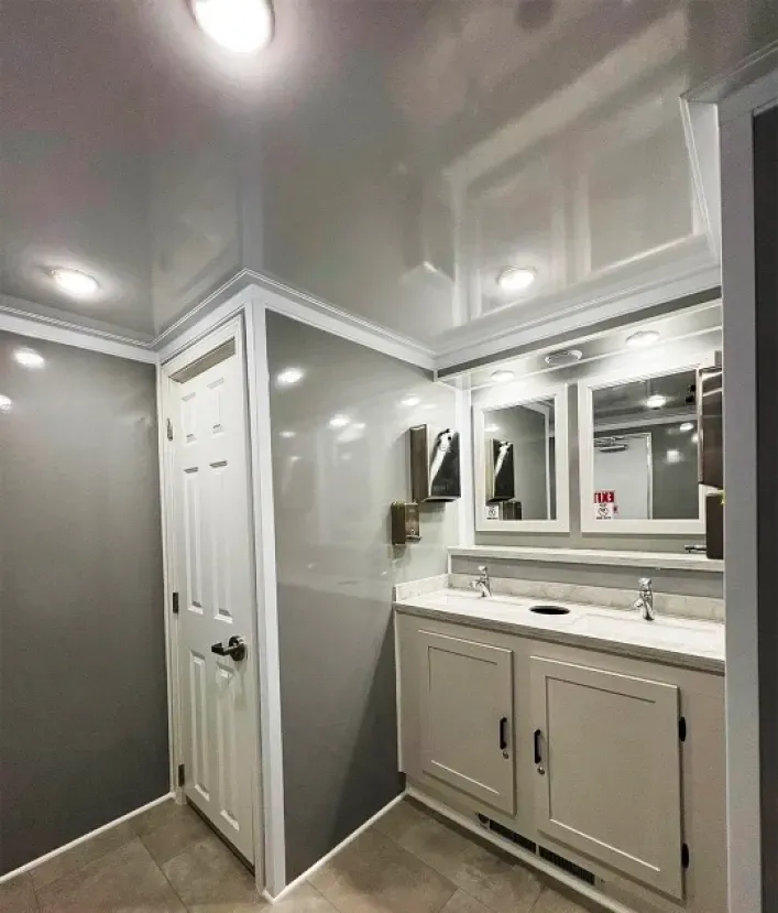 Bright bathroom with gray walls, white vanity, mirror, and shower stall under recessed lights
