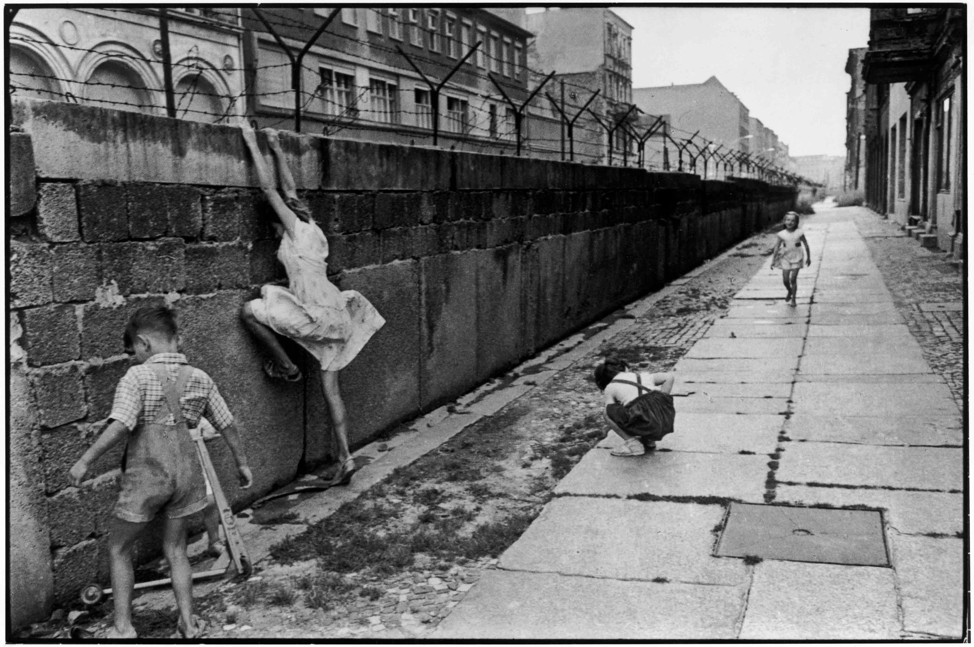 Quastel Associates Valuers | Children playing near the Berlin Wall, one hanging, black and white photo.