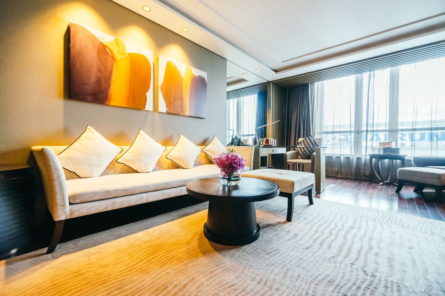 Quastel Associates | Elegant living room with beige sofa, artwork, rug, and large windows.
