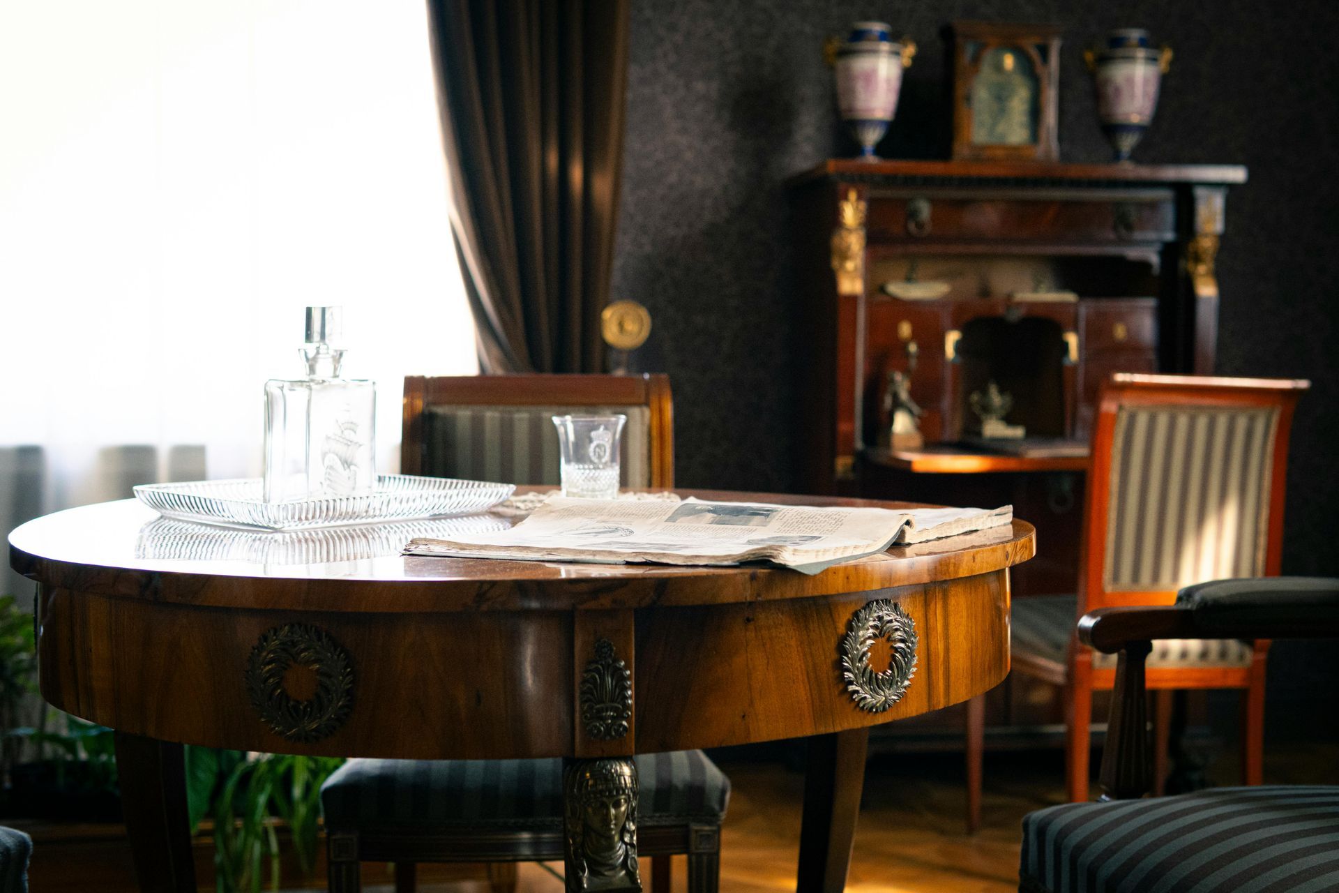 Quastel Associates | a round wooden dining table with a newspaper and glass, set in a dim room. 