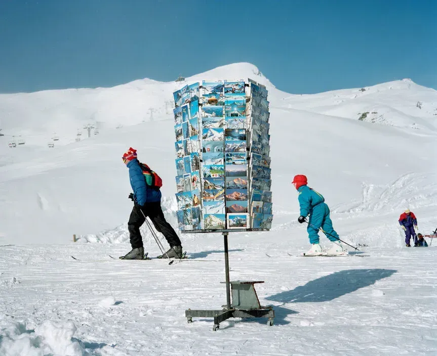 Quastel Associates Valuers | Skiers pass a postcard stand on a snow-covered mountain.