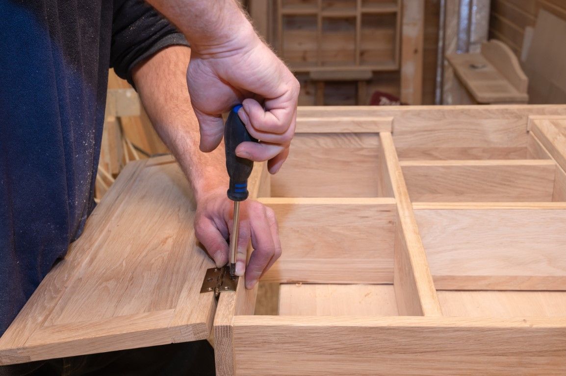 Hands using a hand plane on a wooden cabinet frame in a workshop