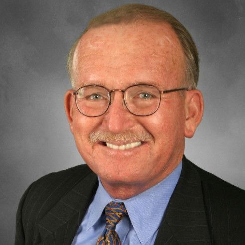 Smiling older man with glasses and mustache, wearing a suit and tie.