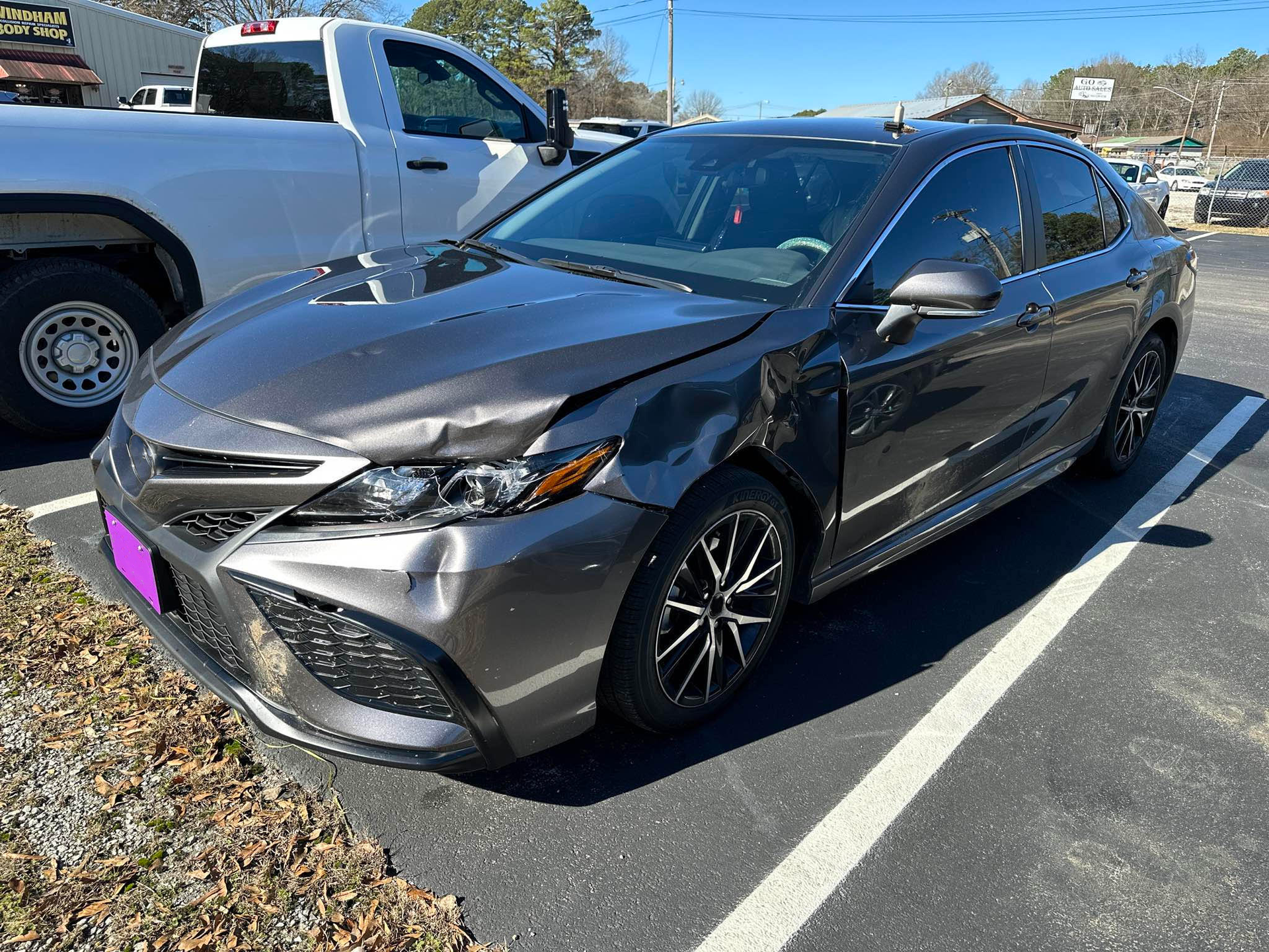 A damaged car is parked in a parking lot next to a truck.  | Windham Bodyshop