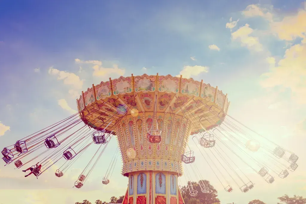Swinging carousel ride against a bright blue sky with sunburst effect.