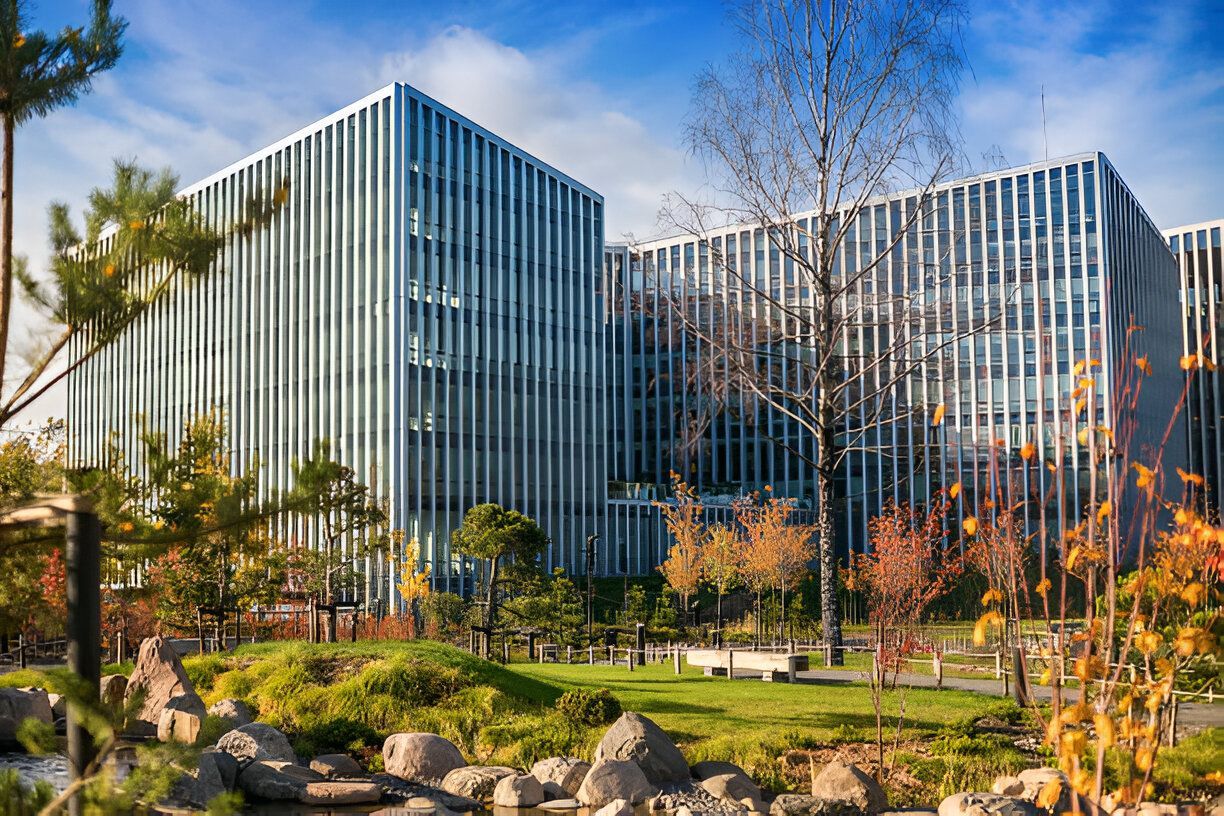 Modern office building with vertical lines and a small park in front with trees and a pond.