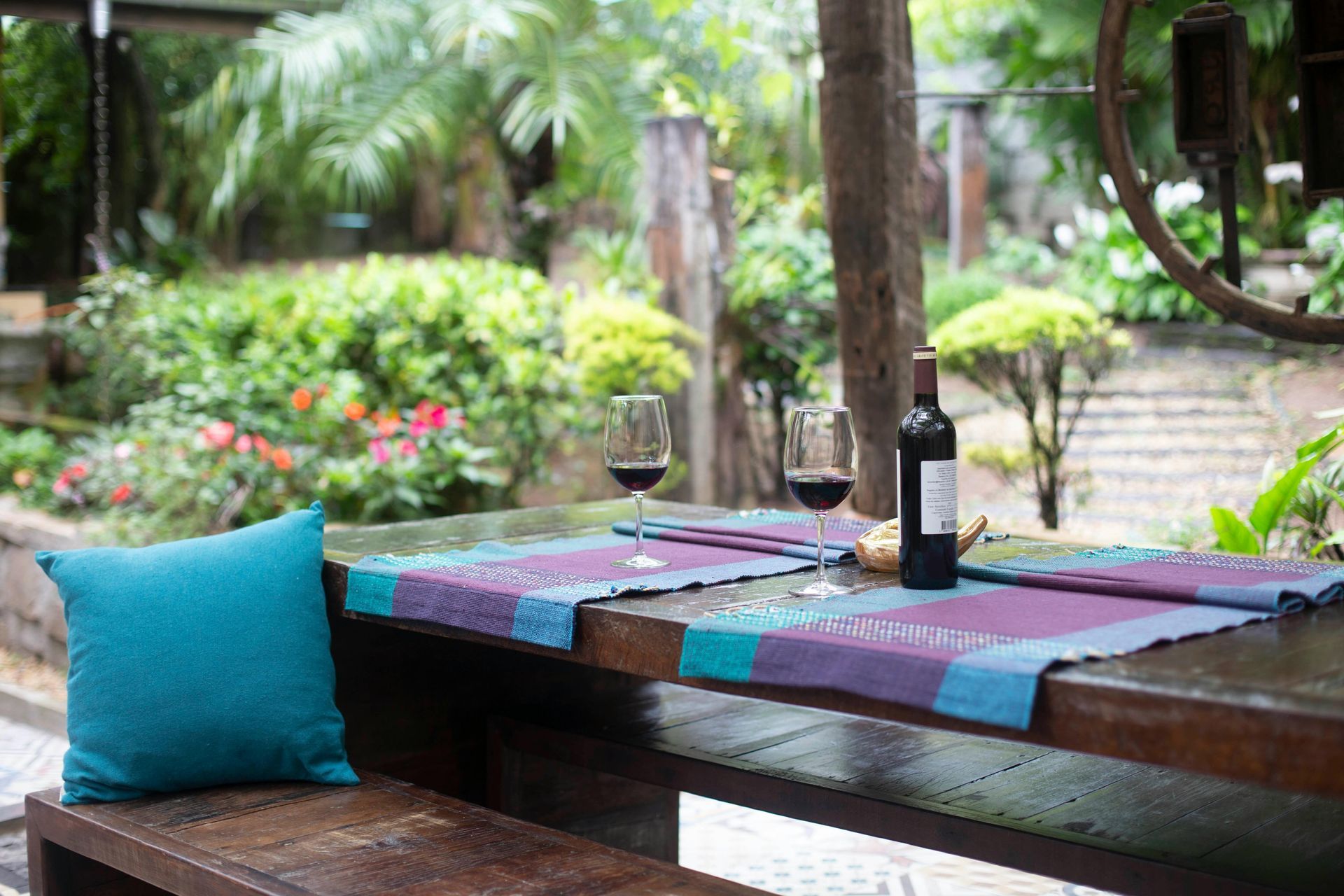 Outdoor table set for wine: red wine bottle and glasses on a wooden table with garden in background.