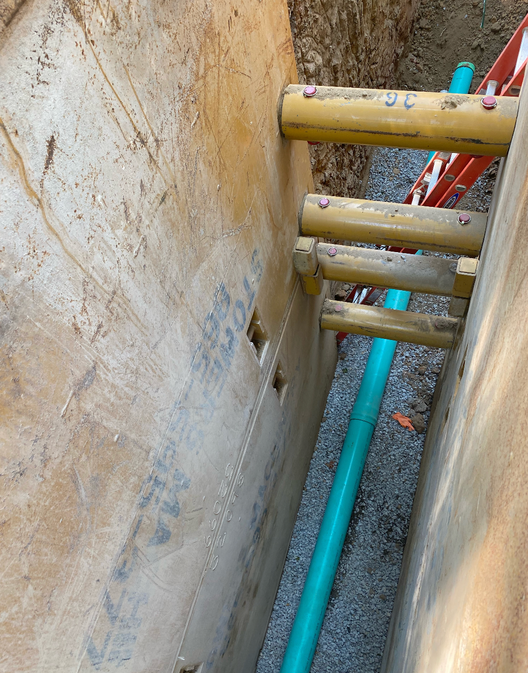 A ladder is sitting in the dirt next to a blue pipe in a trench excavated by Hampton Construction & Development at East Tennessee State University.