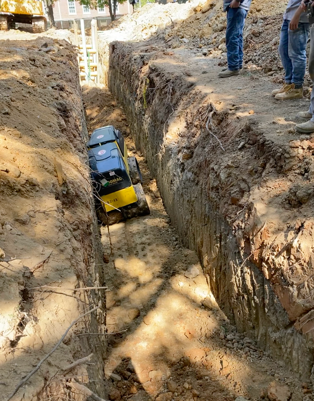 A yellow piece of machinery leveling out a trench in the dirt excavated by Hampton Construction & Development at East Tennessee State University.