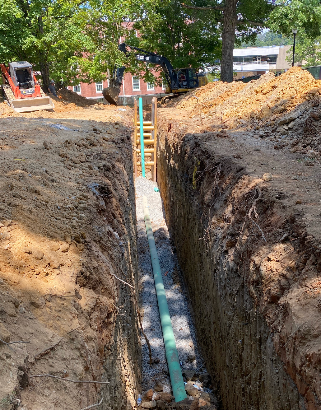 A green pipe is being installed in a trench excavated by Hampton Construction & Development at East Tennessee State University.