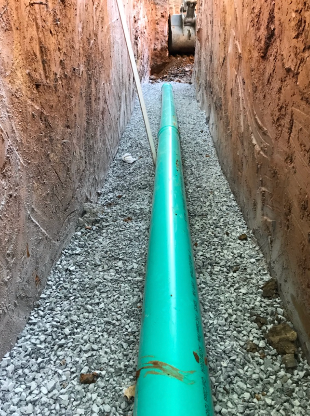 A green pipe is being installed in a trench.
