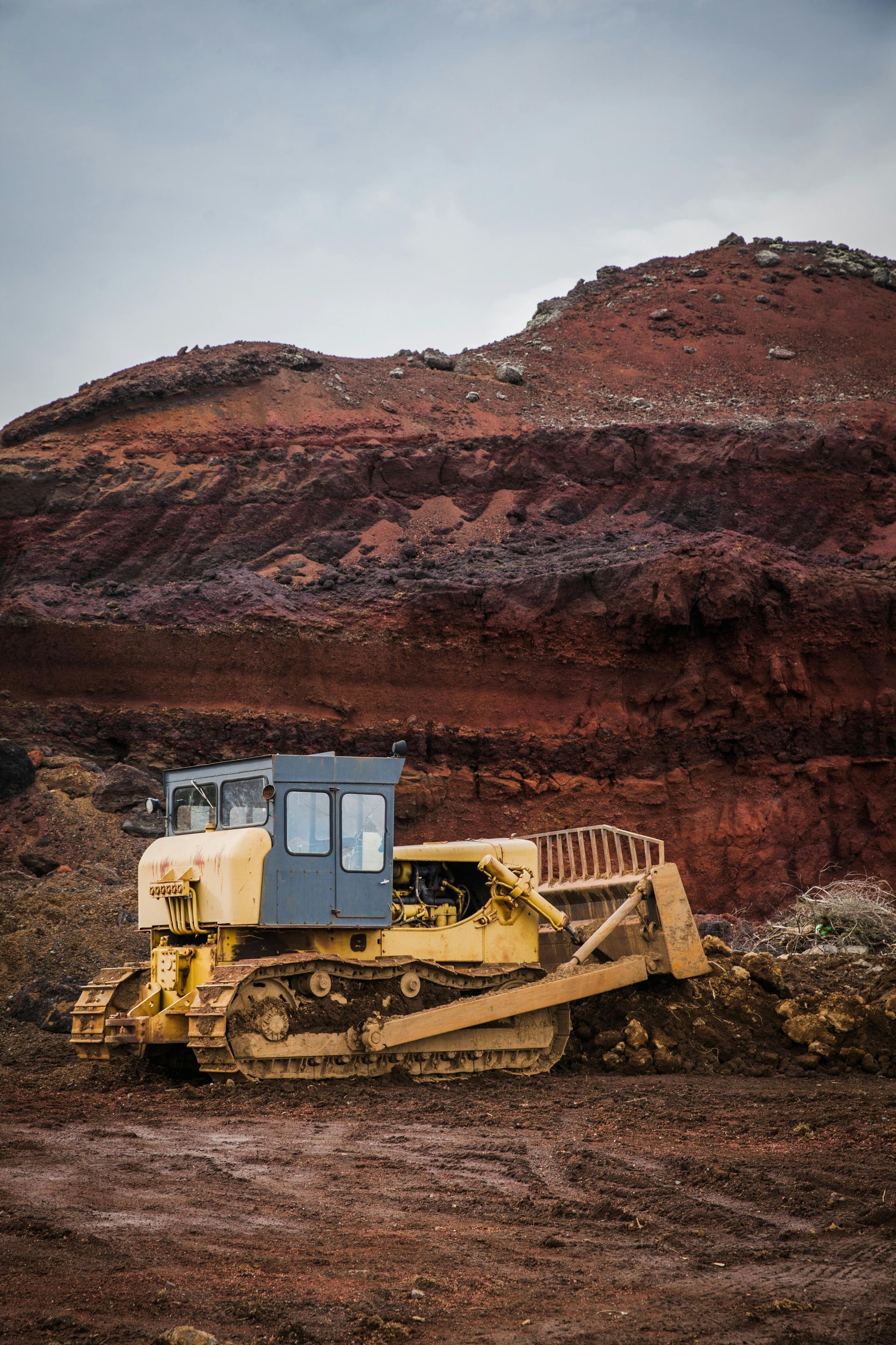 A bulldozer is parked in a dirt field in front of a mountain.