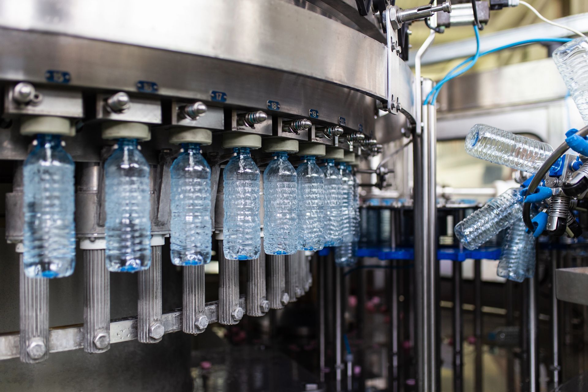 Botellas en una línea de llenado automatizada en una fábrica, con maquinaria metálica y componentes azules.