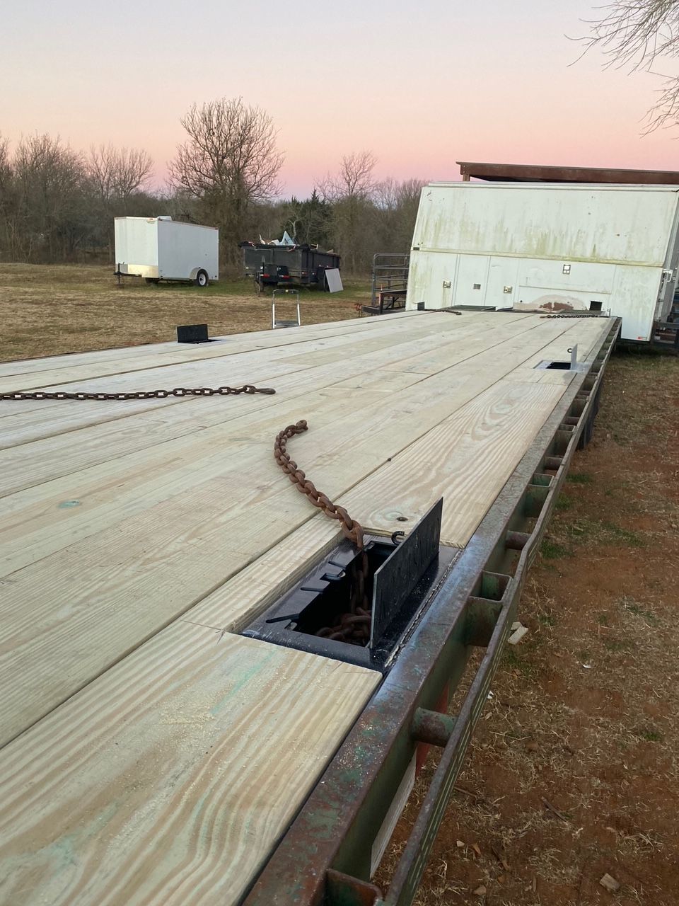 Flatbed trailer with fresh wooden planks, a chain, and a sunset in the background.