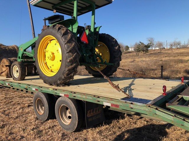 John Deere tractor on a trailer, secured with chains. The setting is outdoors, on a sunny day.