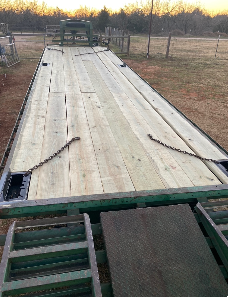 Flatbed trailer with wooden deck, chains, and ramps, set outdoors.