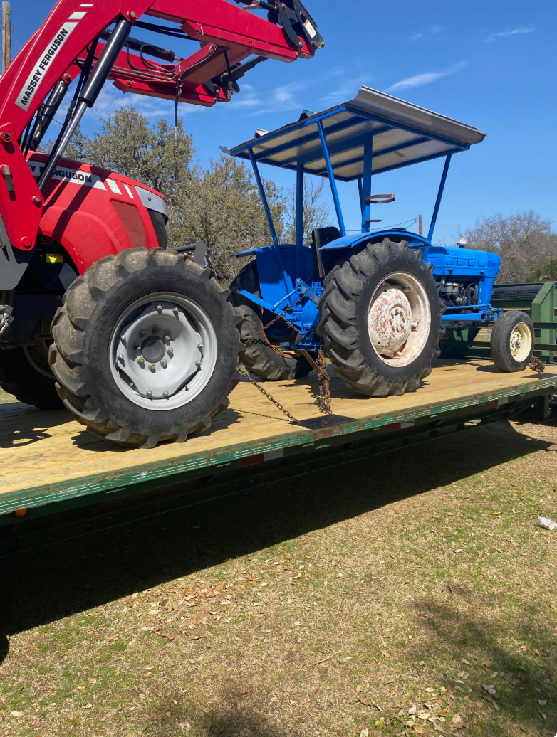 A red tractor with a loader next to a blue tractor on a flatbed trailer outdoors.