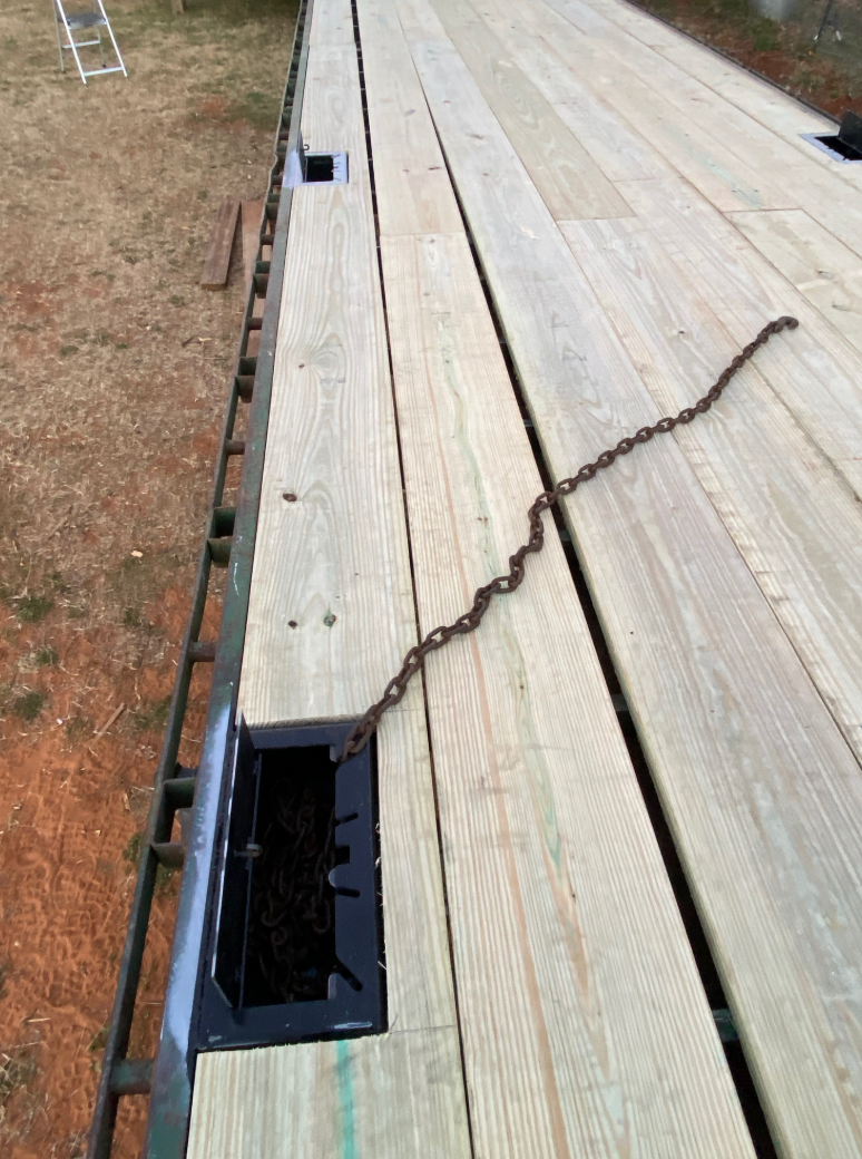 Wooden flatbed trailer with chain lying on the deck near a recessed storage area.