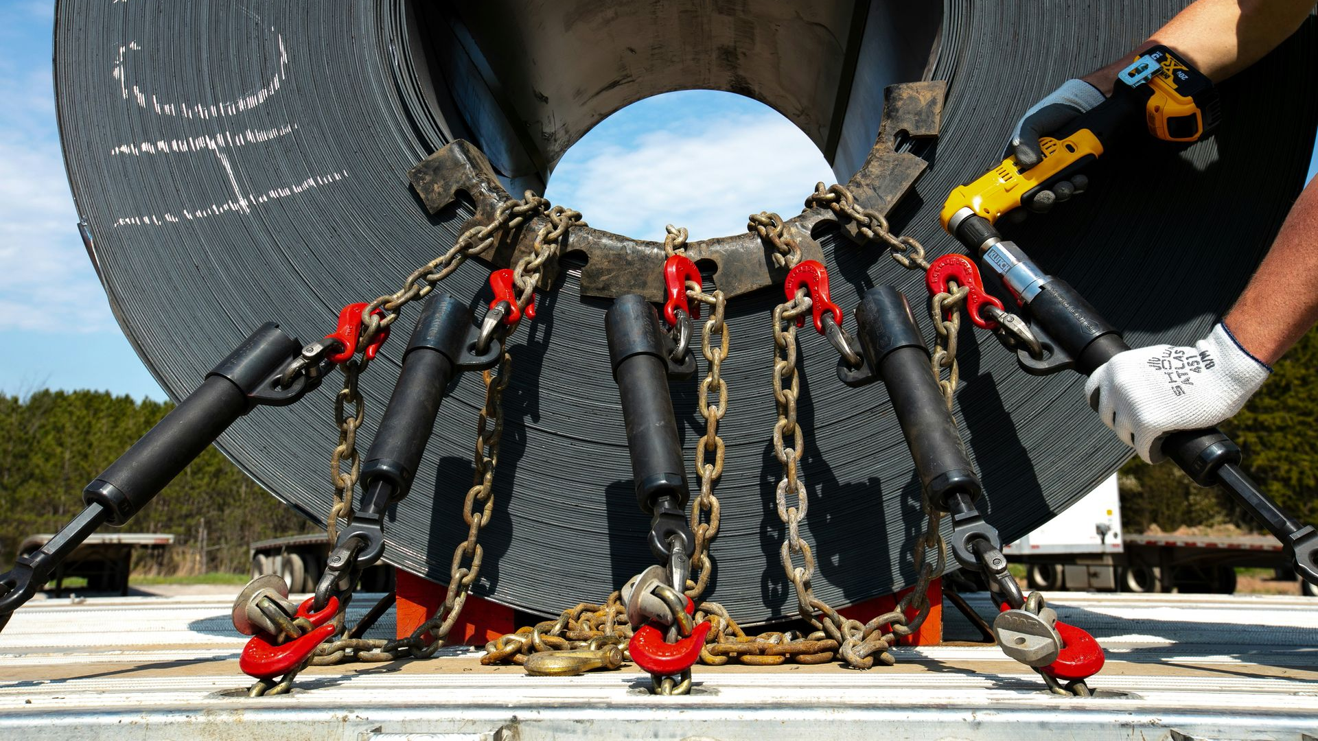 Workers securing a large concrete pipe with chains and clamps at an outdoor construction site