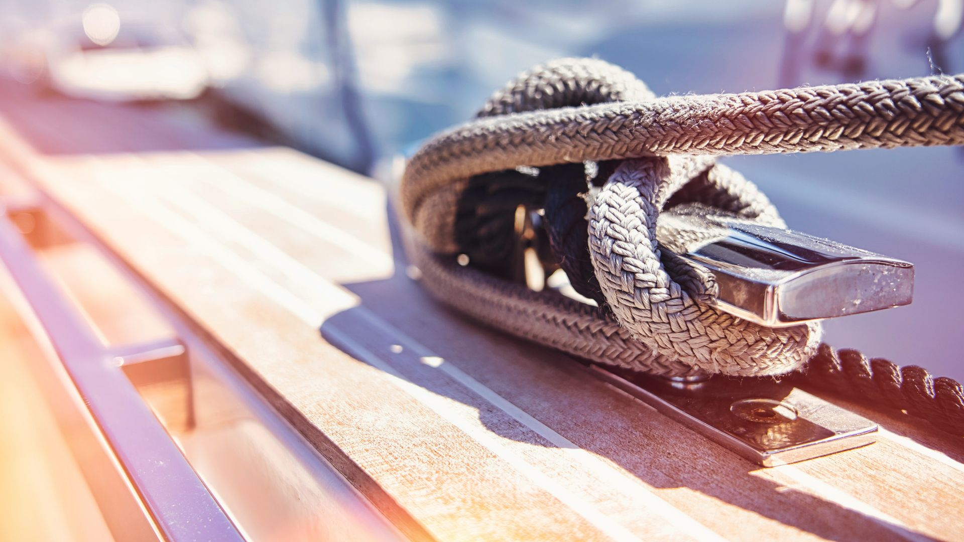 Close-up of a rope cleat on a sunlit wooden boat deck with blurred water in the background