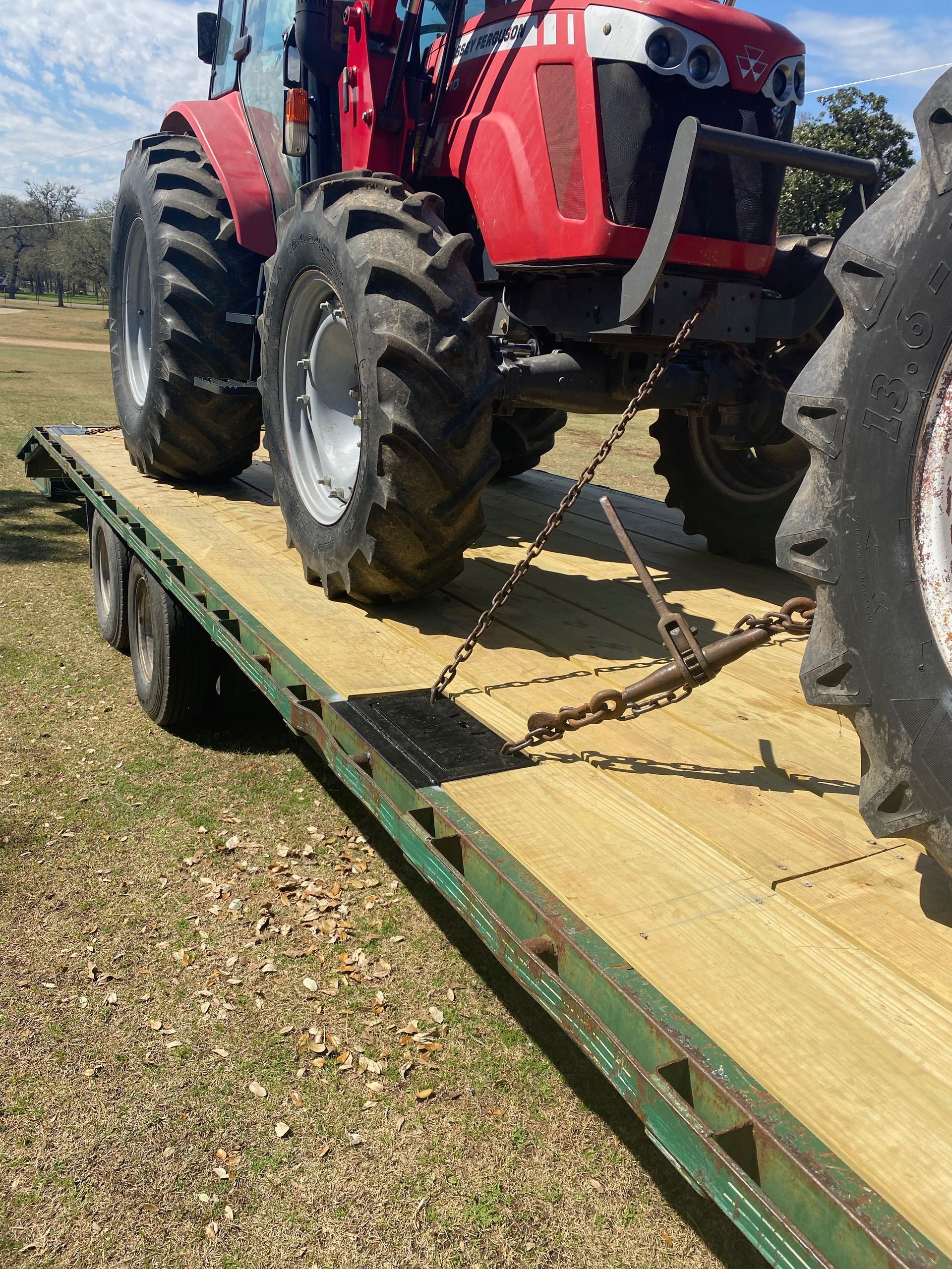 Red tractor secured with chains on a flatbed trailer on a grassy field.