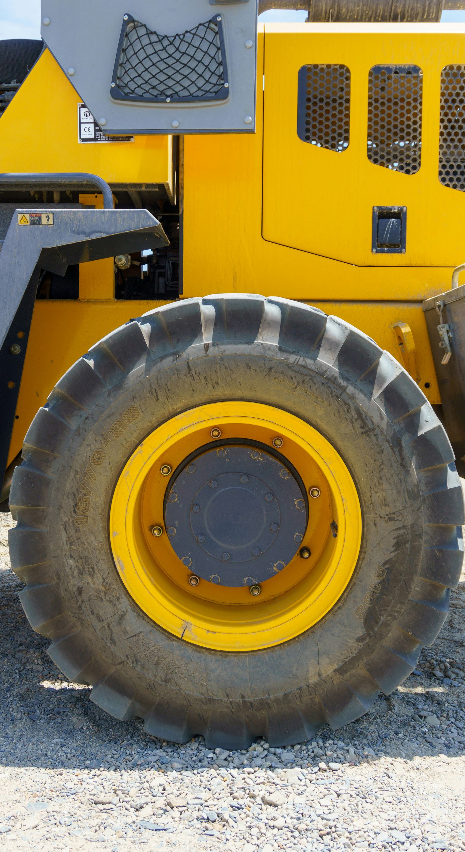 Close-up of a yellow construction vehicle wheel on gravel, with a black tire and yellow rim.