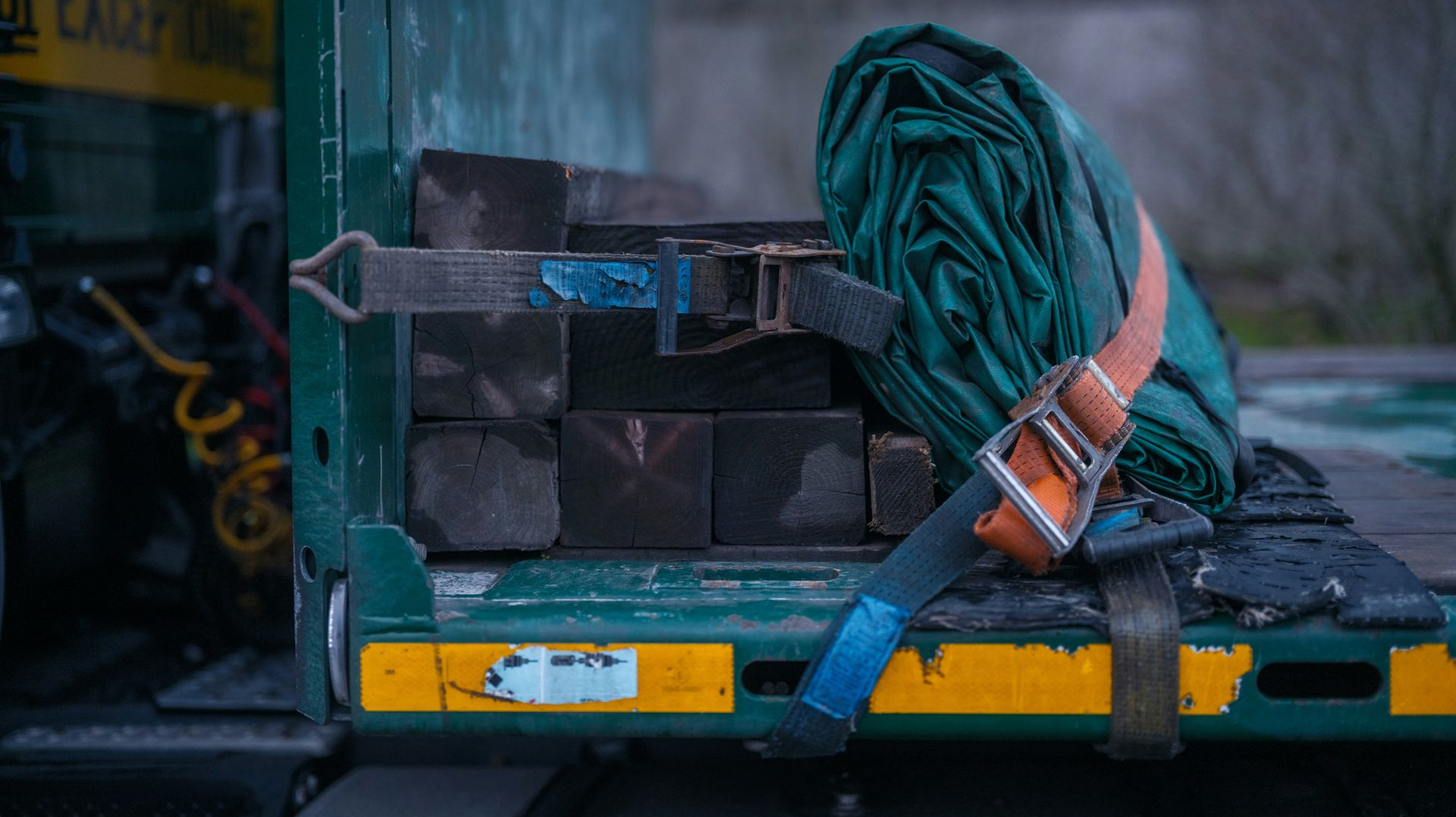 Coiled green hose secured with a tan strap on the back of a truck bed with metal boxes.