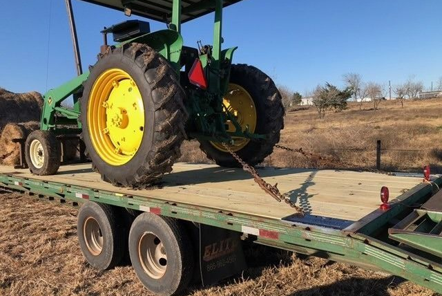 A green and yellow John Deere tractor loaded on a flatbed trailer in a field.