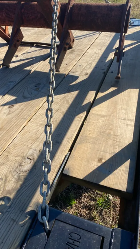 A metal farm implement is secured with a chain to the wooden deck of a flatbed trailer.