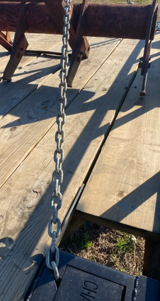 A metal chain hangs vertically from a black tool box mounted on the wooden deck of a trailer, near a rusty metal frame.