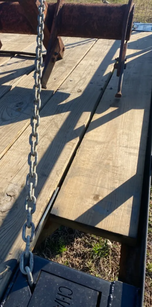 Two tractors are secured with chains to the bed of a flatbed trailer outdoors on a sunny day.