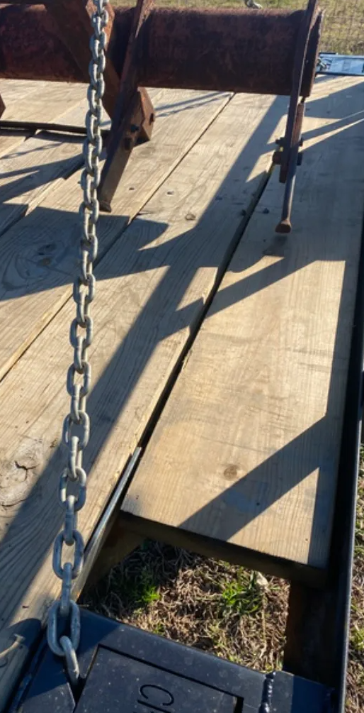 Worn metal gate with chain and railing across a concrete walkway in sunlight