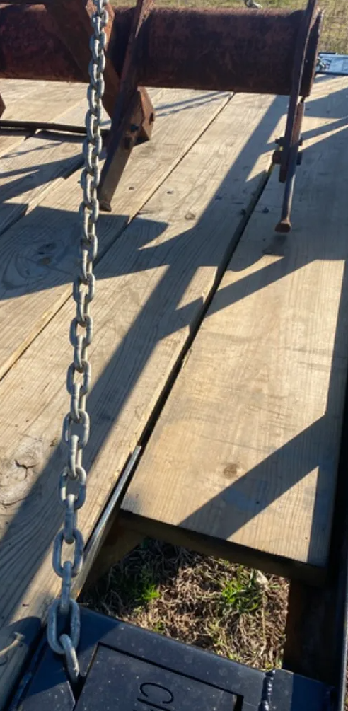 Worn metal gate with chain and railing across a concrete walkway in sunlight