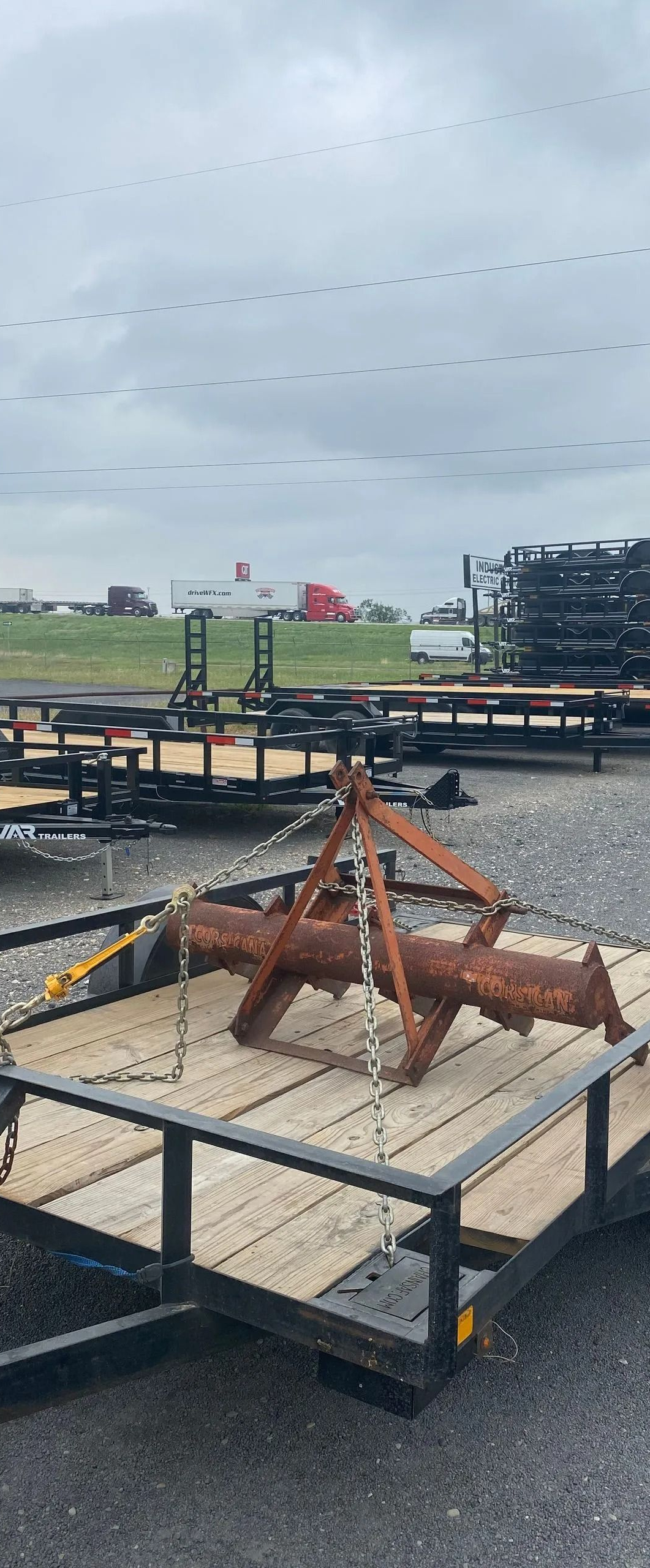 A metal chain with a red binder attached, connected to a steel tie-down point on a wooden trailer floor.